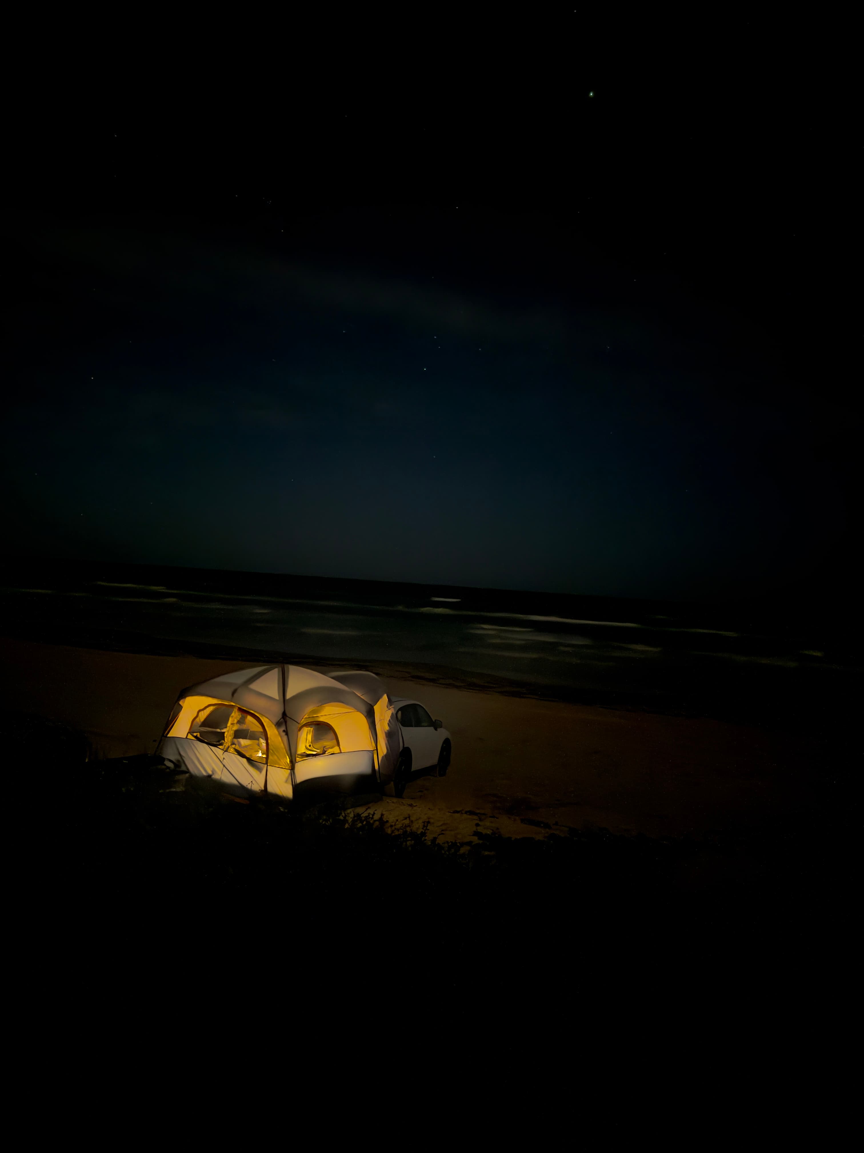 Tent glowing beside the ocean at night.